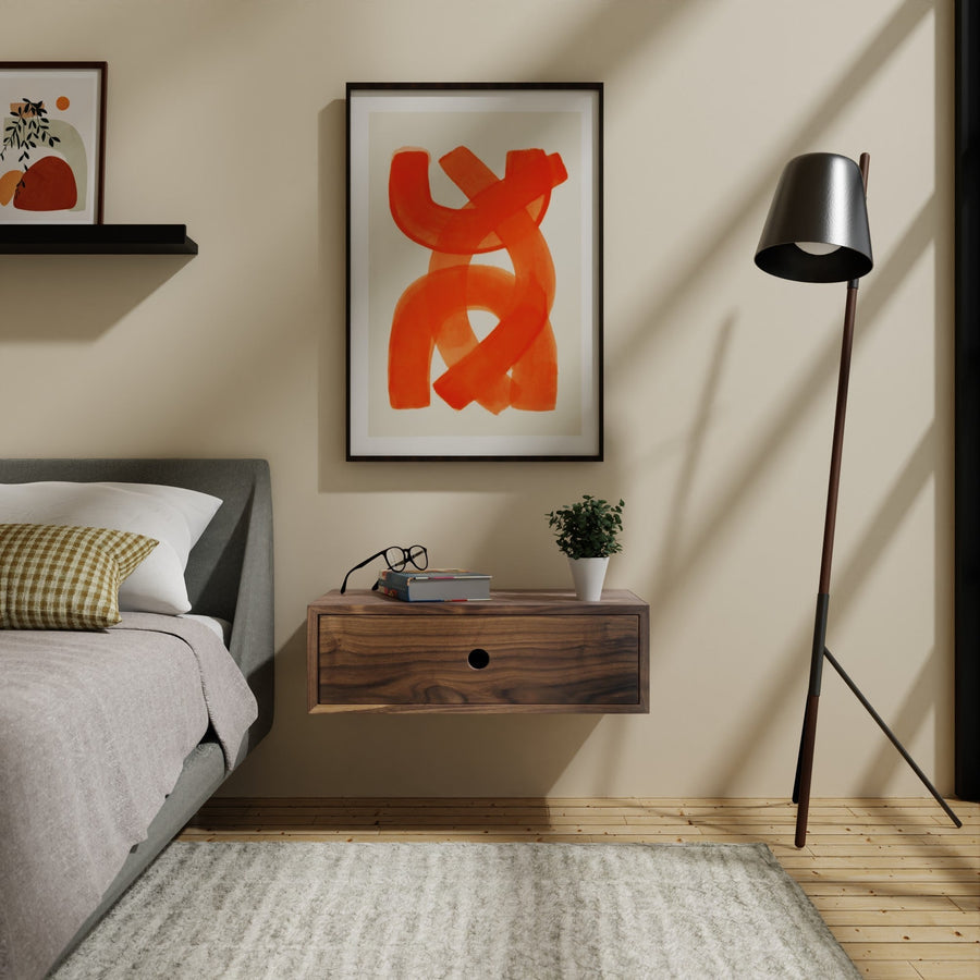 A modern bedroom with a cozy bed, a Krovel Furniture Co. hardwood floating nightstand holding glasses and a small plant, and a colorful abstract painting on the wall. A slim floor lamp adds elegance as sunlight casts shadows on the wooden floor and light beige walls.