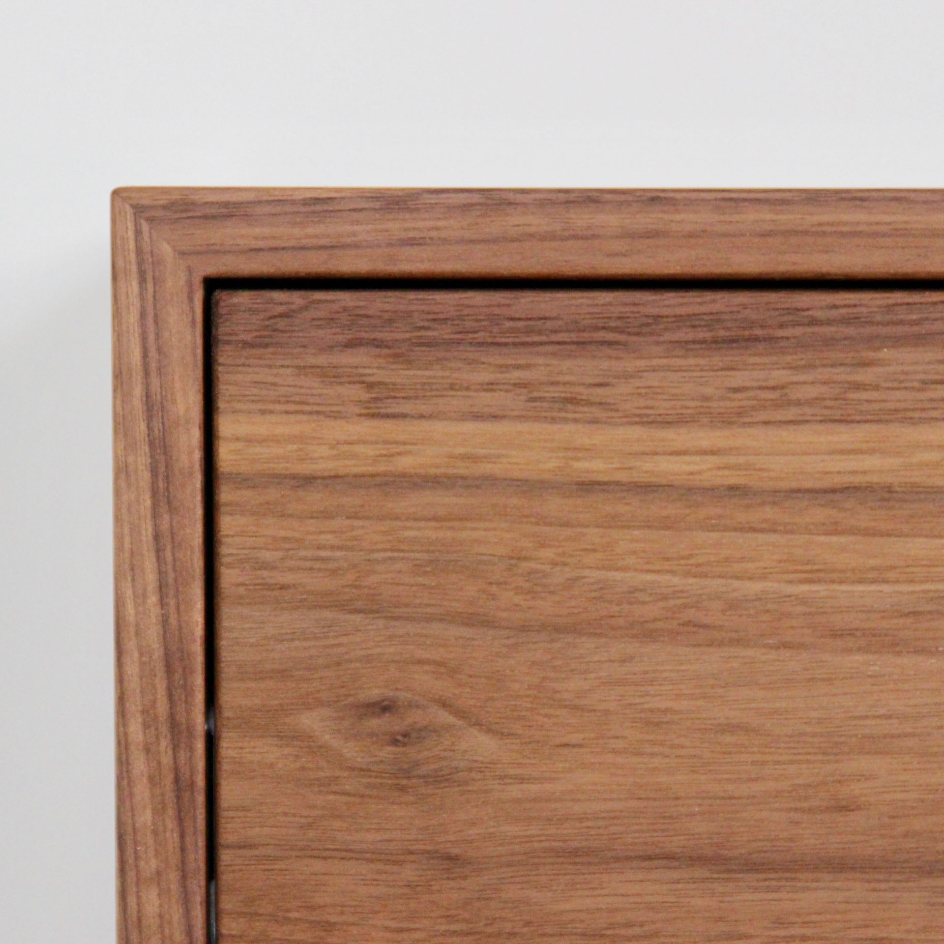 A close-up of a wooden cabinet corner, showcasing the smooth grain and natural texture of the wood. Handmade by Krovel Furniture Co., this piece embodies a simple, modern design with clean lines and a light brown finish.