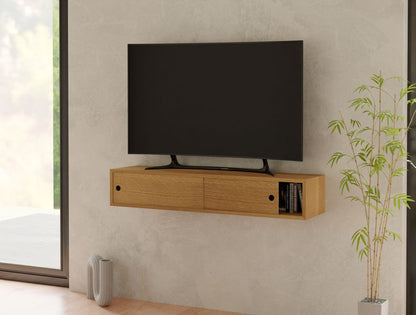 A minimalist living room corner features a flat-screen TV mounted on a light-colored wall above a Krovel Media Console Table in White Oak. The console has small openings perfect for books and decor. Nearby, a bamboo plant adds a touch of greenery, while natural light floods in from a large window.