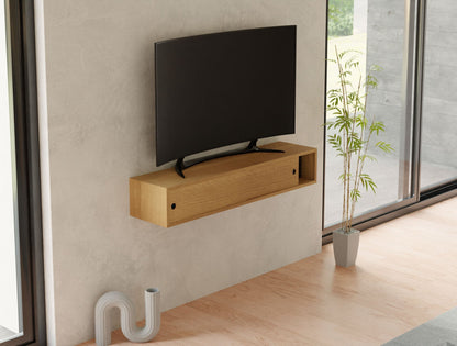 A minimalist living room showcases a wall-mounted flat-screen TV on a Krovel Media Console Table in White Oak. Nearby, a small potted plant sits on the light wood floor, while large windows with views of greenery add to the tranquil ambiance.