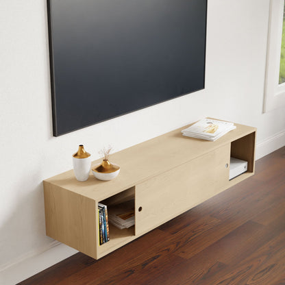 A minimalist living room showcasing the Krovel Oversized Media Console Table in Maple below a large, flat-screen TV. The console table elegantly displays books, a magazine, and decorative vases. The dark wood floor beautifully complements the space beside the window on the right.