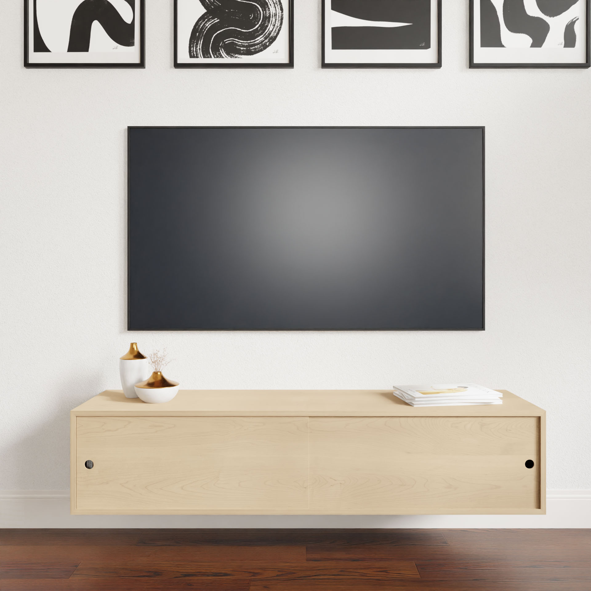 A minimalist living room features a Krovel Oversized Media Console Table in Maple, beautifully hand-finished with a smooth light wood appearance. Above it, a sleek black wall-mounted TV is displayed. The console is adorned with decorative bowls and neatly arranged papers, while the pristine white wall is enhanced by striking abstract black-and-white art pieces.