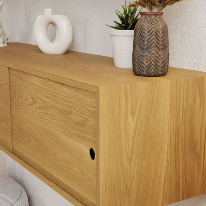 The Oversized Media Console Table in White Oak by Krovel features a sleek design with sliding doors and circular handles, beautifully complementing the white round vase, small potted succulent, and tall vase with a textured leaf pattern displayed on it. Its elegant style is highlighted against the neutral-colored wall.