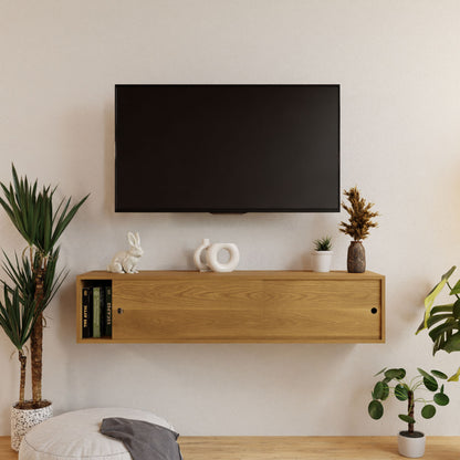 In a modern living room, a TV is mounted on a white wall above the elegant Krovel Oversized Media Console Table in rich White Oak. The console is securely hung with a French cleat and displays decorative items like plants and books. Nearby, a pouf sits beside a tall plant for added style.