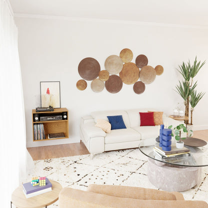 A modern living room features a white sofa, colorful cushions, and a wall adorned with round wooden decorations. The Krovel Record and Stereo Storage Cabinet in solid American cherry hosts the record player. A large potted plant and a glass coffee table with books rest on a patterned rug, exuding mid-century modern charm.