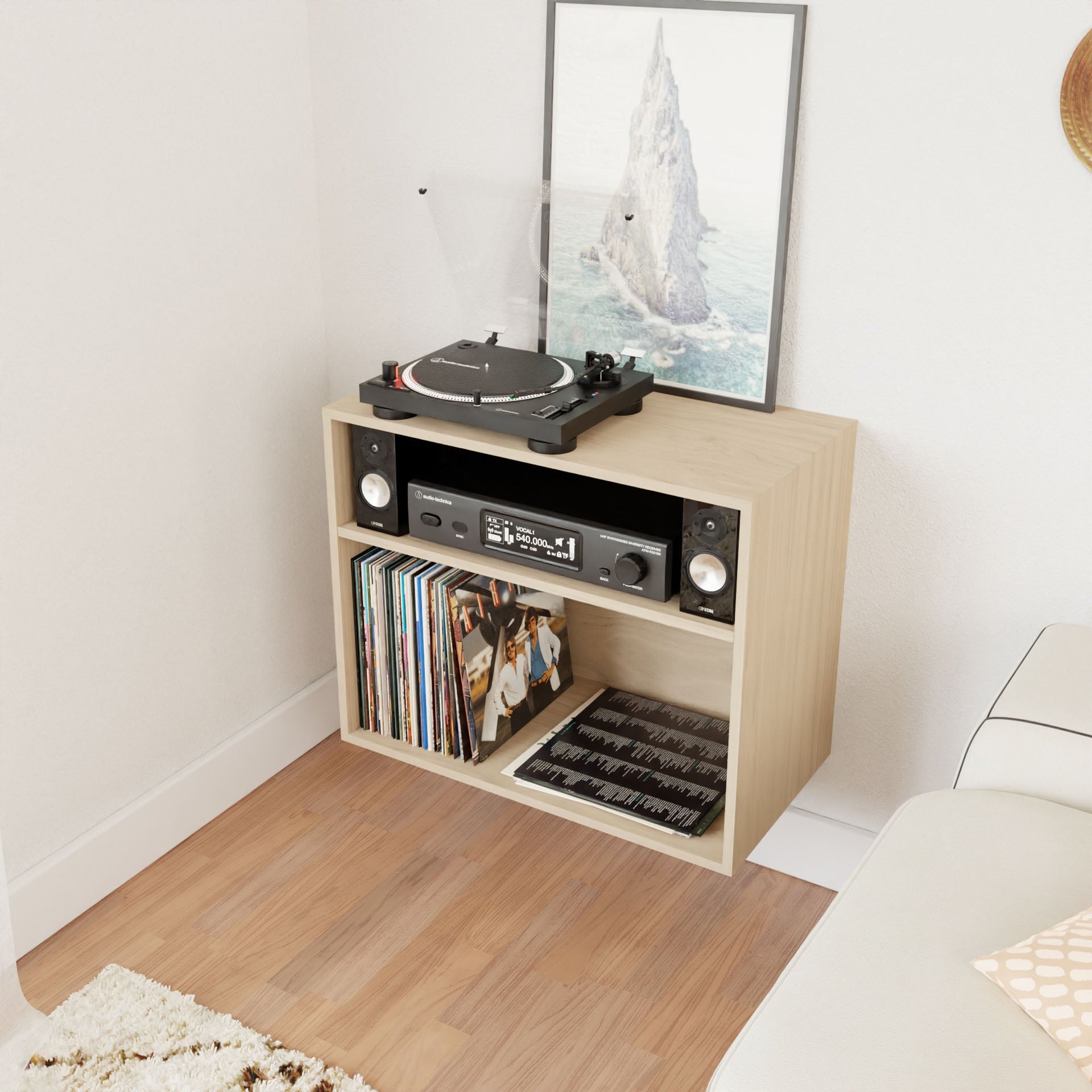 The Krovel Record and Stereo Storage Cabinet in Maple features a compact design that supports a turntable on top, accompanied by a framed picture of a mountain. Below, the stereo system is complemented by small speakers. The bottom shelf is filled with vinyl records, adding mid-century modern charm to the cozy room corner.