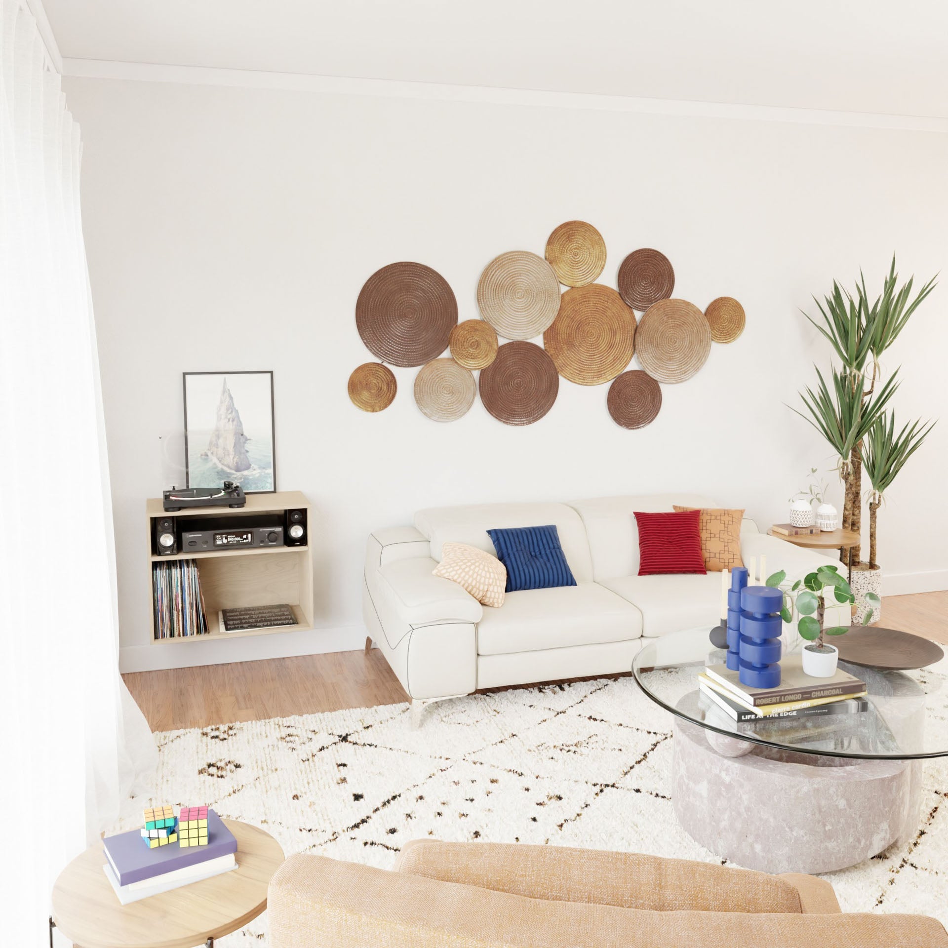 A modern living room features a white corner sofa adorned with colorful cushions, complemented by a circular glass coffee table. The wall is accented with round woven decor, and a tall plant in the corner brings vitality to the space. A Krovel Record and Stereo Storage Cabinet in Maple serves as an elegant Mid-Century Modern console table, stylishly supporting a record player and displaying a framed picture nearby.