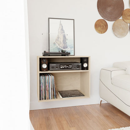 A Record and Stereo Storage Cabinet in Maple by Krovel stands in the living room, featuring a contemporary design reminiscent of Mid-Century Modern furniture. It supports a record player with speakers, an amplifier, and a vinyl record collection. A framed artwork depicting a rocky peak is showcased nearby, accompanied by woven wall decorations adorning the adjacent white wall.