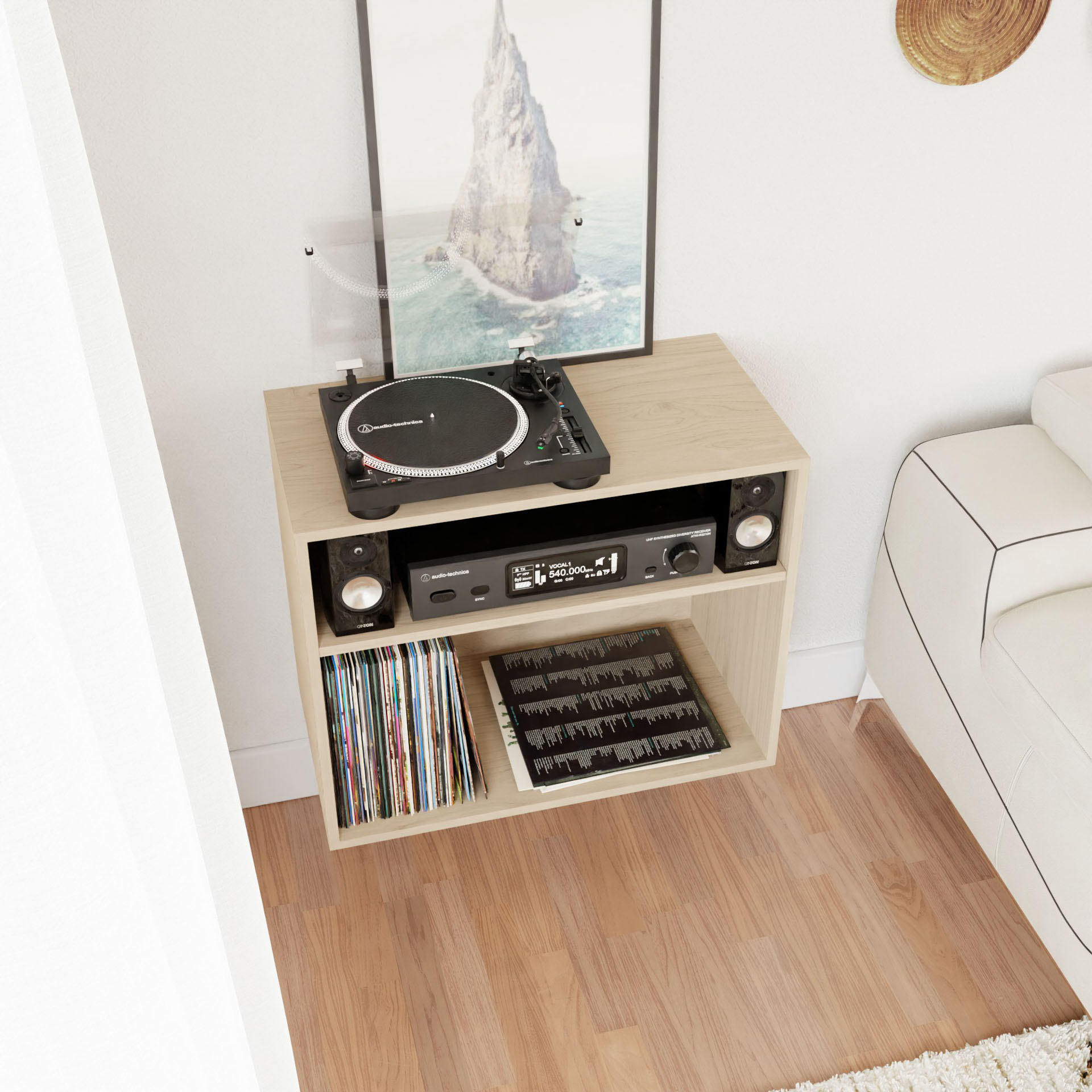 A mid-century modern shelf unit, Krovel's Record and Stereo Storage Cabinet in Maple, crafted from rich maple wood, houses a record player, stereo receiver, and vinyl records. A large framed seaside photograph leans against the wall above the stereo console table. This arrangement is situated next to a white sofa on a cozy wooden floor.