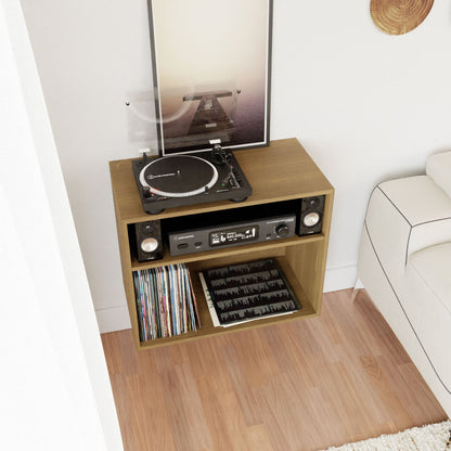 A Record and Stereo Storage Cabinet in White Oak by Krovel rests on a hardwood floor, featuring a turntable on top. Below, it houses sleek mid-century modern stereo components with speakers and provides space for vinyl record storage. To the right, part of a white couch is visible.