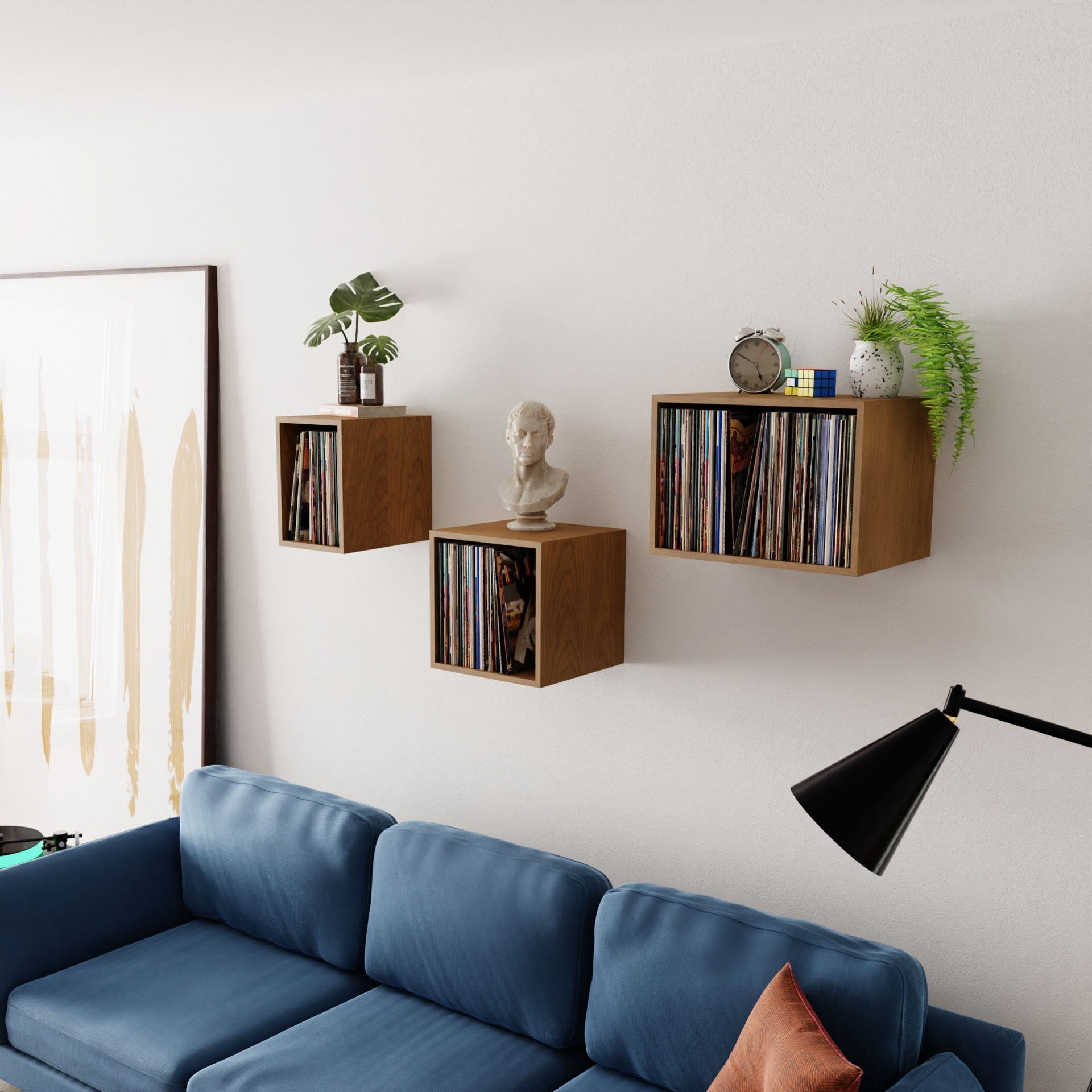 In a contemporary living room, a blue couch is paired with a sleek black floor lamp, while three Record Storage Shelves in Cherry from Krovel elegantly display a vinyl collection, a bust, a globe, and potted plants. A large abstract painting embellishes the white wall.