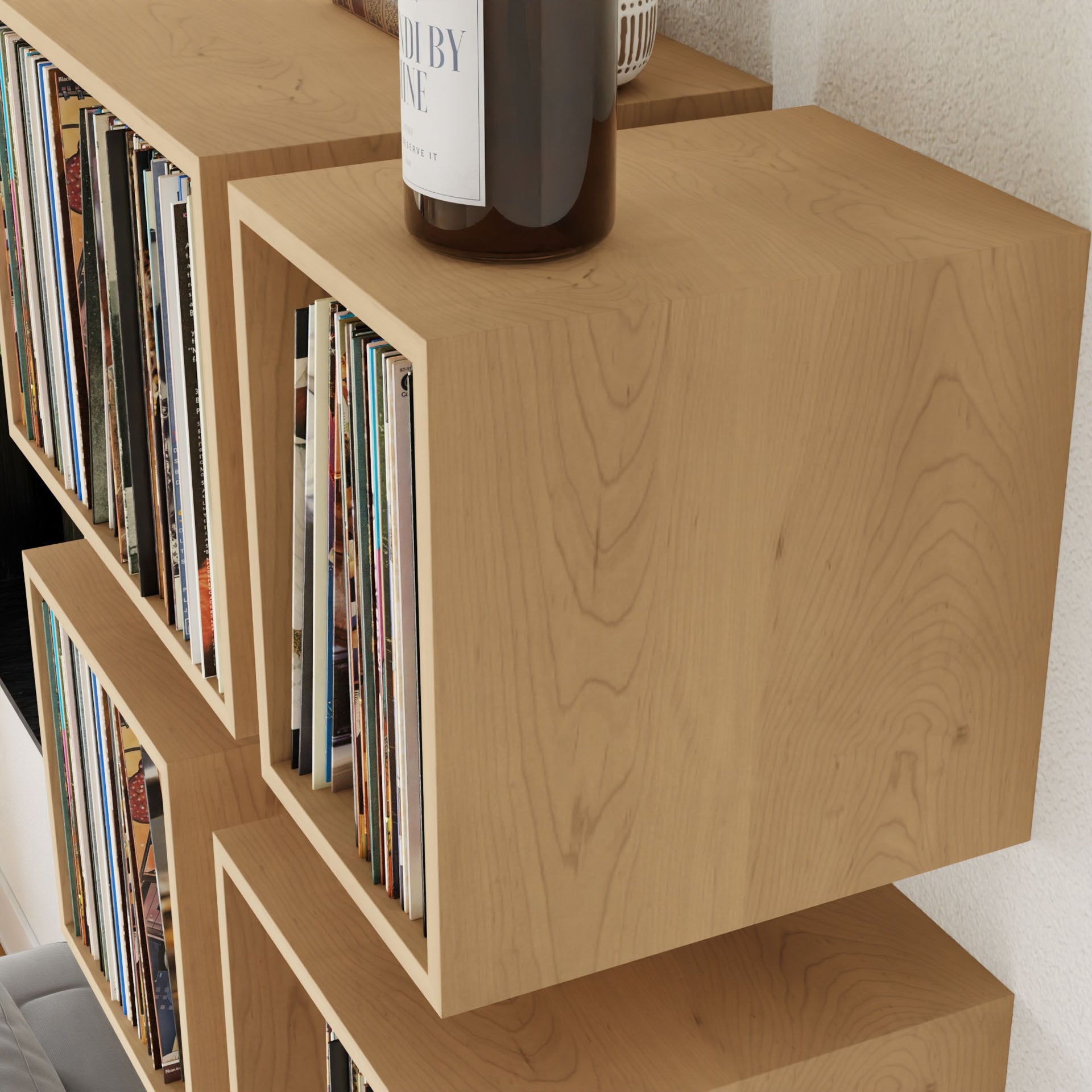 A set of Record Storage Shelves in Maple by Krovel, mounted on the wall, showcases a vinyl collection. A brown bottle sits atop these floating shelves, with their natural wood grain adding a warm, mid-century modern aesthetic to the room.