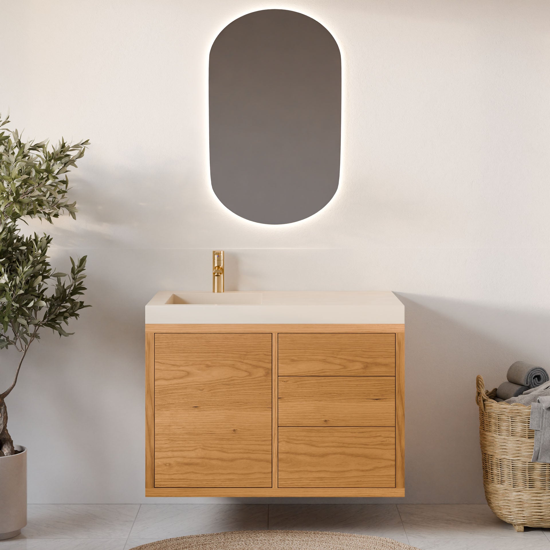 A minimalist bathroom features a floating Krovel Furniture Co. Single Door, Triple Drawer Vanity in Cherry with soft-close drawers and gold faucet. An oval mirror adorns the wall, a potted plant rests on the left, and a woven basket with towels is on the right for a serene ambiance.