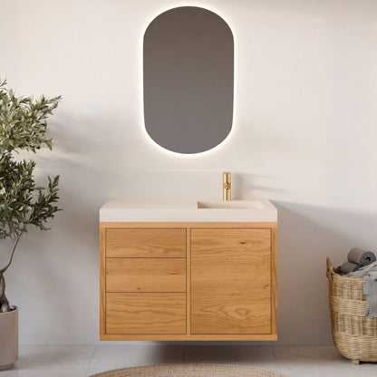 A minimalist bathroom showcases a cherry-colored vanity by Krovel Furniture Co., featuring a single door and three soft-close drawers. A modern oval backlit mirror complements the scene, with a gold faucet on the white countertop, greenery on the left, and an organized wicker towel basket on the right.