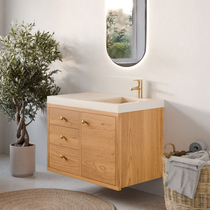 A minimalist bathroom showcases Krovel Furniture Co.'s Single Door, Triple Drawer Vanity in Cherry with a white sink. Gold fixtures add elegance, and an oval mirror hangs above. Nearby, a wicker basket with rolled towels complements a small potted tree on the light floor.