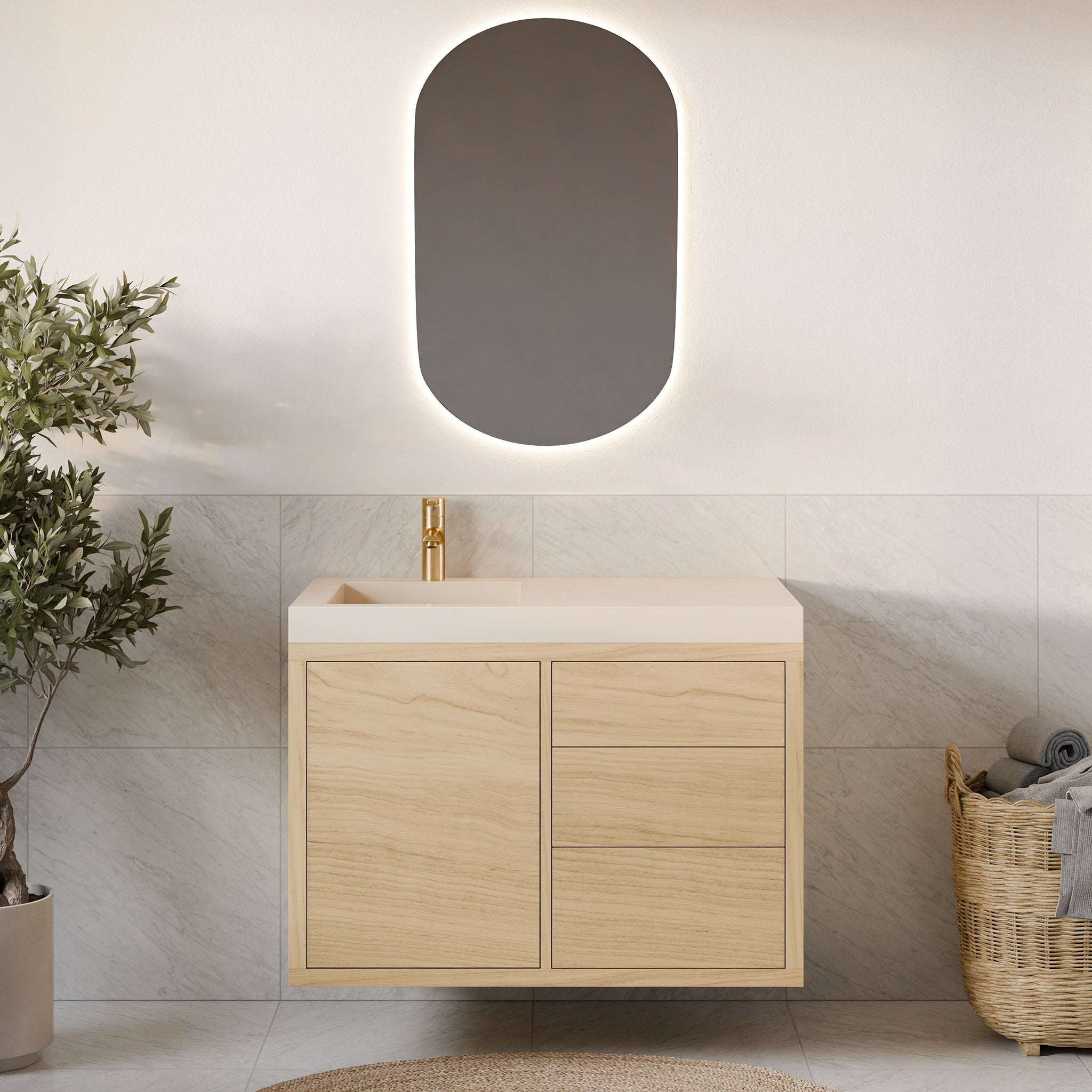 A modern bathroom showcases a Krovel Furniture Co. Single Door, Triple Drawer Vanity in Maple, complemented by a gold faucet and an oval mirror with soft backlighting. Light gray tiles, white-painted walls, and a basket of towels with a small plant complete the homely touches.