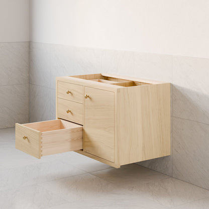 The Single Door, Triple Drawer Vanity in Maple by Krovel Furniture Co. is a wall-mounted floating bathroom vanity with a light hardwood veneer. It includes four soft-close drawers, one open to reveal a spacious interior, against wall tiles with a light marble-like pattern.