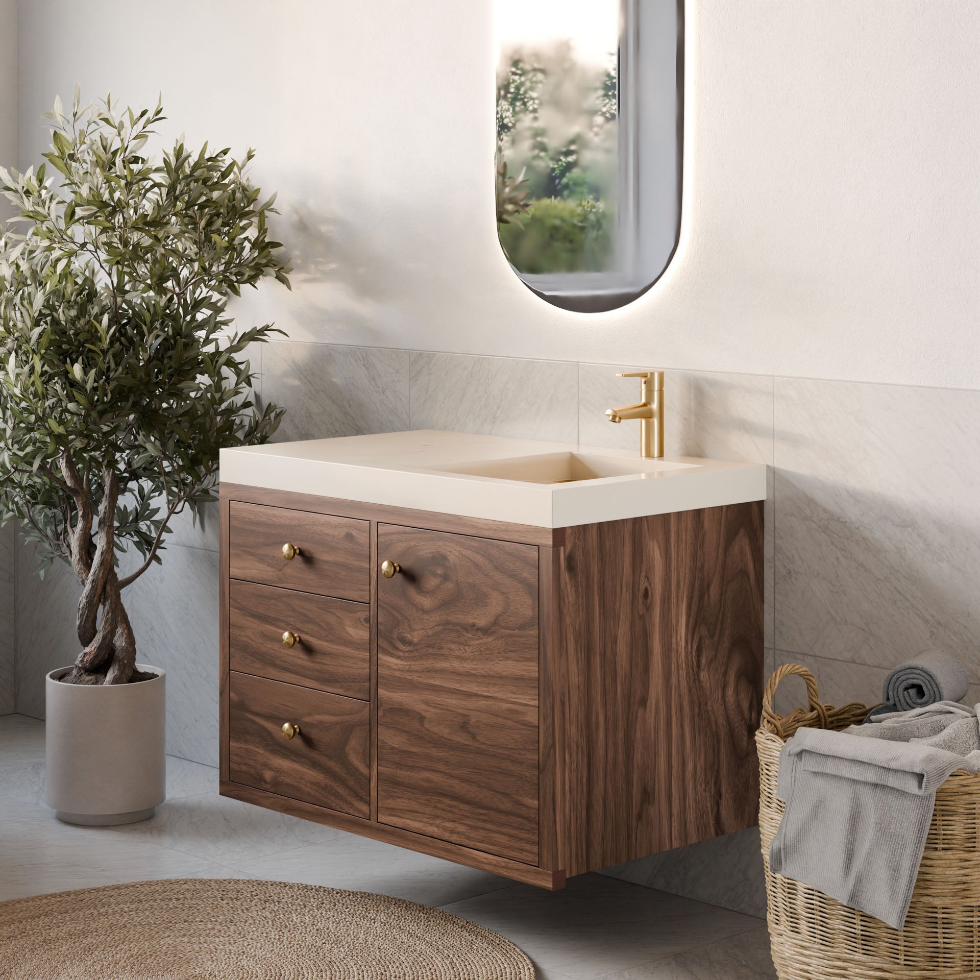 A modern bathroom features Krovel Furniture Co.'s single door, triple drawer vanity in walnut with a beige countertop. Enhanced by soft-close hinges and a gold faucet, the space includes a large oval mirror, potted plant, and woven basket with rolled towels in serene natural light.