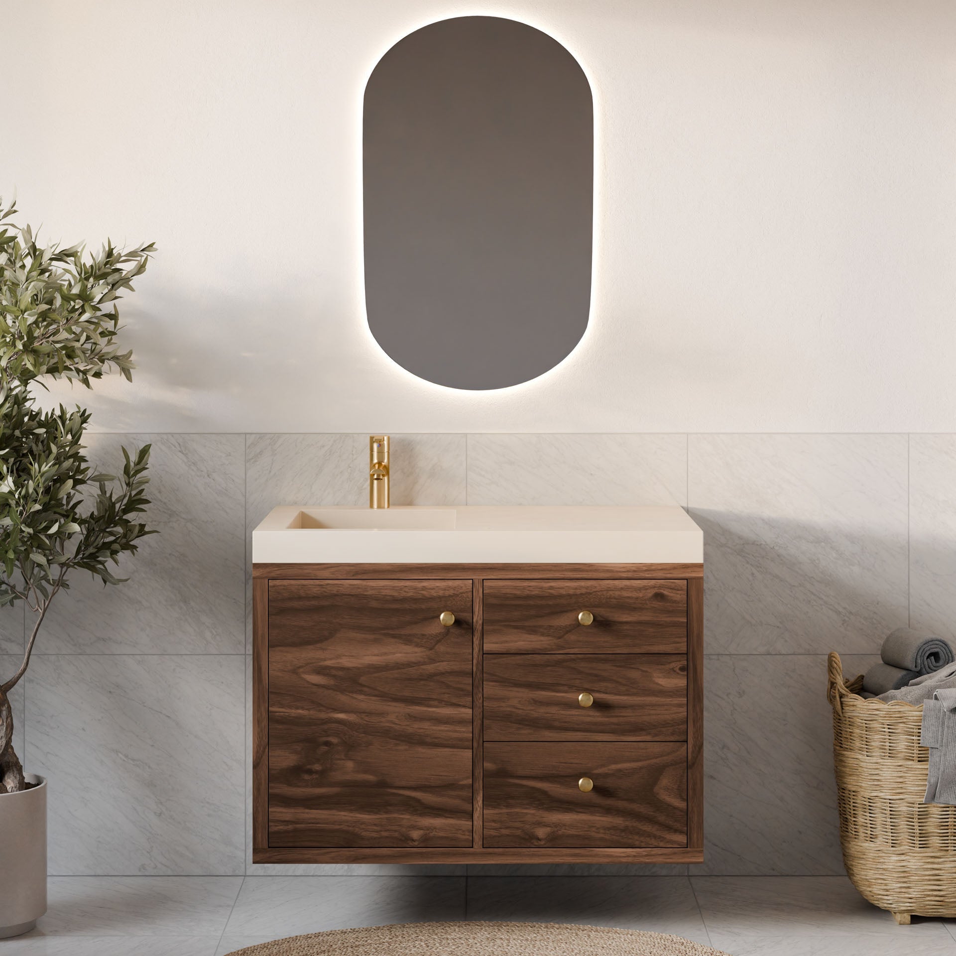 A minimalist bathroom showcases Krovel Furniture Co.'s Single Door, Triple Drawer Vanity in Walnut with gold faucets under an oval mirror. The vanity features gold handles and soft-close drawers. A potted plant and wicker basket with towels sit against a white tiled wall background.#configuration_left-side-sink