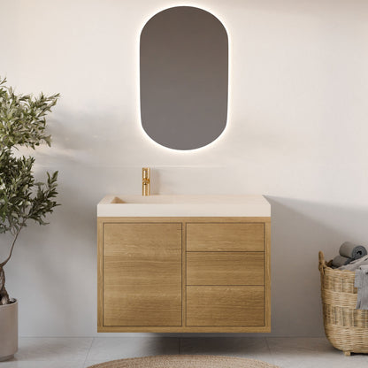 The bathroom showcases Krovel Furniture Co.'s Single Door, Triple Drawer Vanity in White Oak beneath an oval backlit mirror. Featuring soft-close drawers and a gold faucet on the beige countertop, it is flanked by a wicker basket with rolled towels on the right and a potted plant on the left.