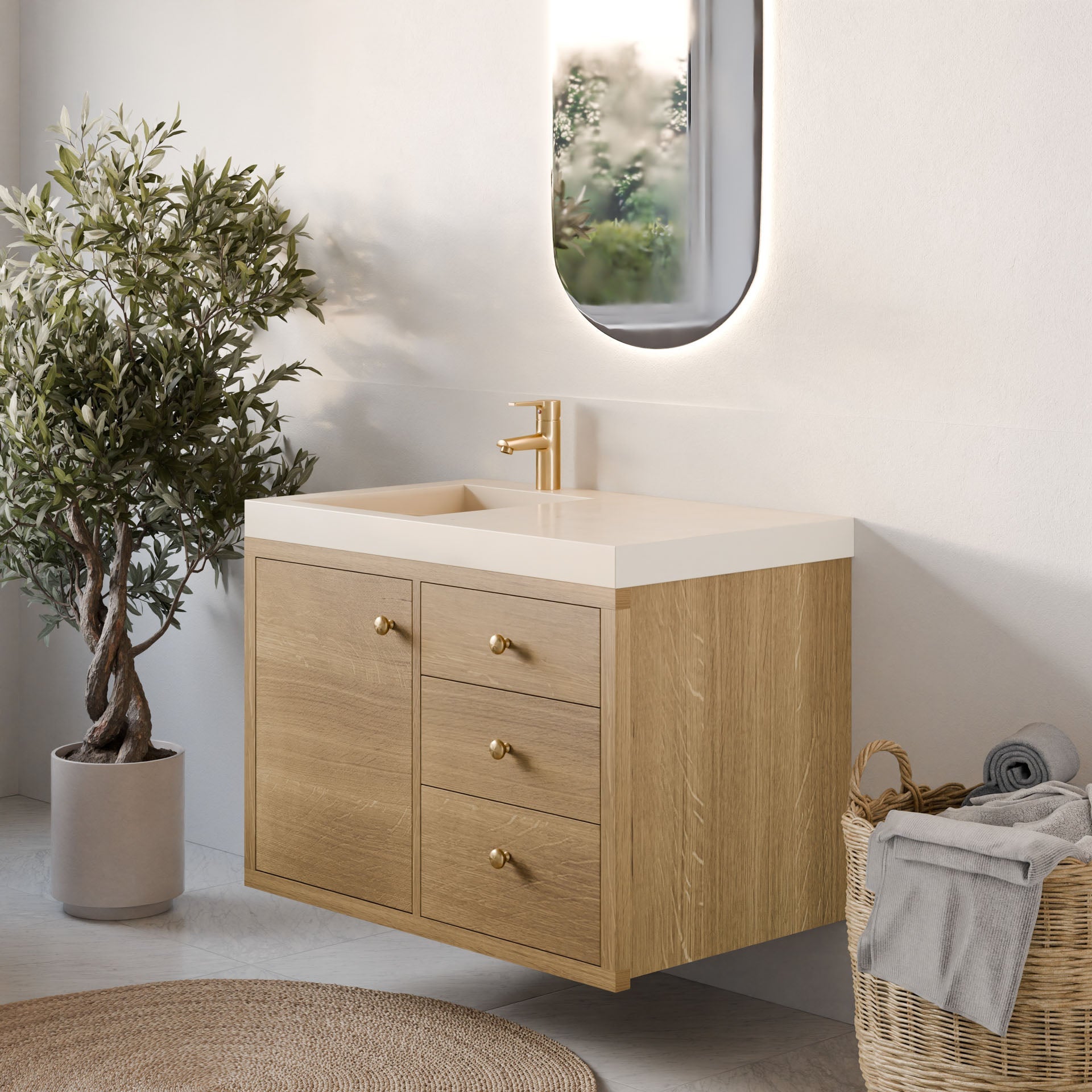 A modern bathroom showcases Krovel Furniture Co.'s Single Door, Triple Drawer Vanity in White Oak with gold fixtures and a sleek white sink. An oval mirror hangs above, surrounded by a basket of towels. A potted plant adds greenery as sunlight streams through the window, casting gentle shadows.