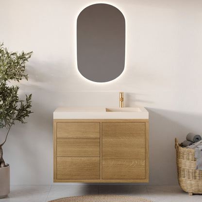 A minimalist bathroom showcases Krovel Furniture Co.'s Single Door, Triple Drawer Vanity in White Oak with soft-close hardware and a rectangular sink. An oval mirror with backlighting hangs above, complemented by a wicker basket with towels and a potted plant, set against light walls and flooring.