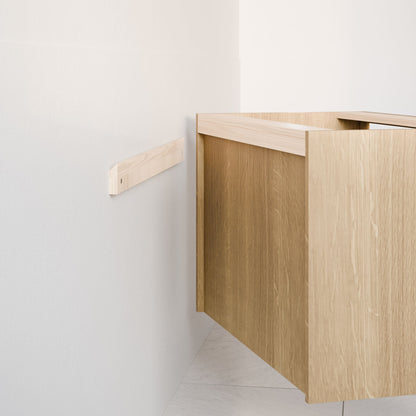 A partially installed Krovel Furniture Co. Single Door, Triple Drawer Vanity in White Oak is seen against a light wall, displaying only its side and top. A wooden bracket aligns the vanity for mounting, with light tile flooring enhancing the modern aesthetic.