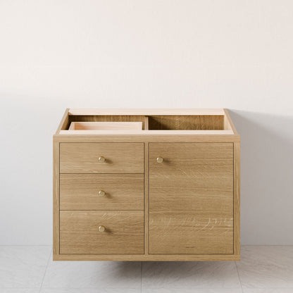 The Single Door, Triple Drawer Vanity in White Oak by Krovel Furniture Co. showcases a minimalist wooden design. It includes three soft-close drawers on the left, a door-compartment on the right with round metal knobs, and an unfinished top that complements its hardwood veneer.