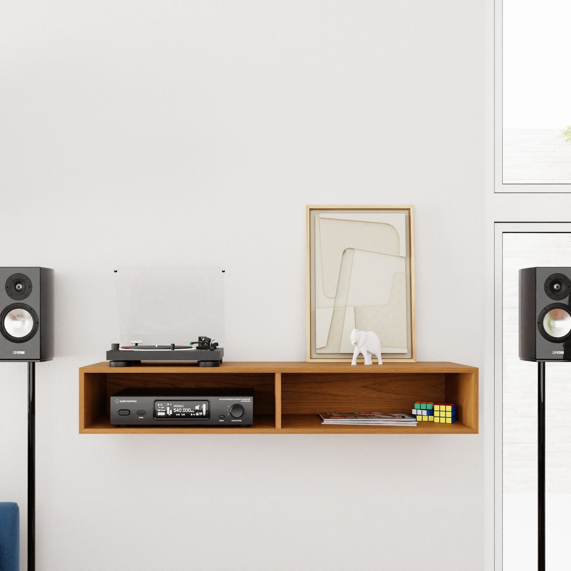 A minimalist room showcasing the Krovel Stereo Table in Cherry, styled as a mid-century modern wooden wall shelf. It holds a turntable, vintage radio, abstract art, a small sculpture, and a Rubik's cube. The arrangement is complemented by two speakers on stands against a white wall with a window.