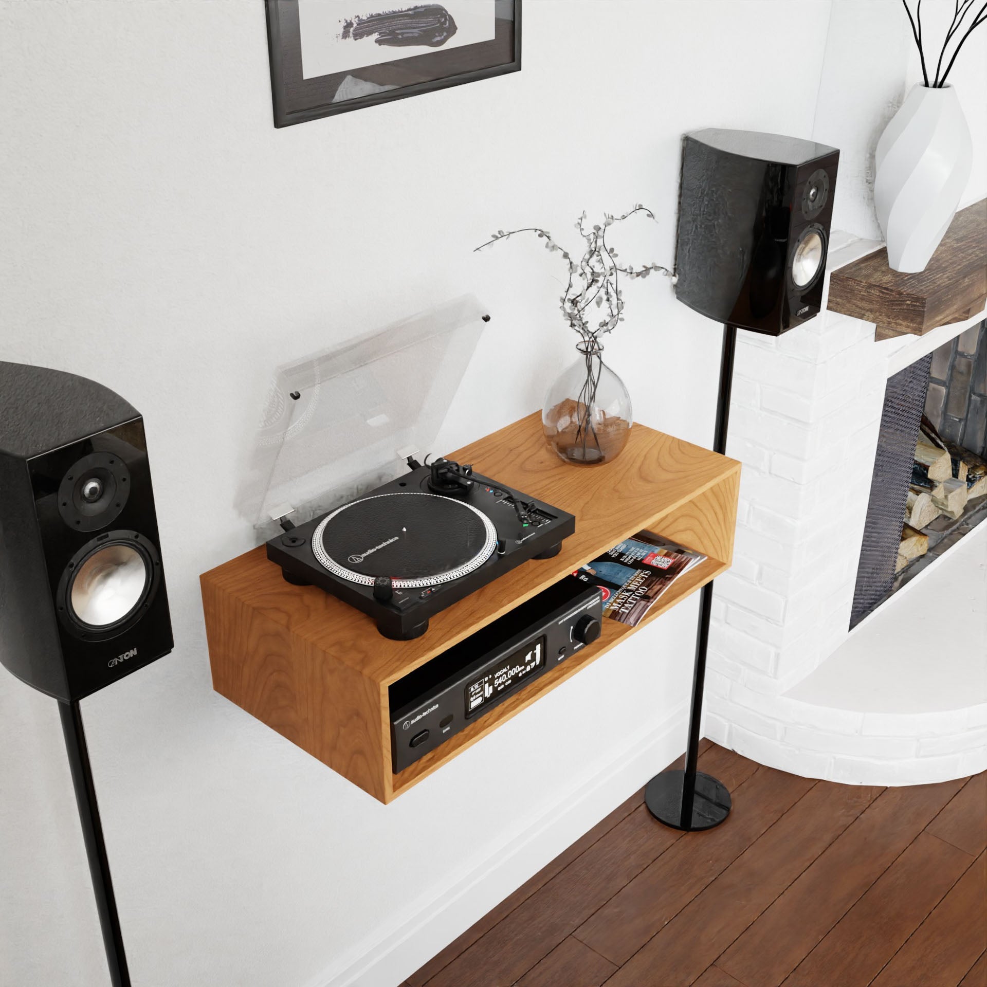 A modern living room showcases the Krovel Stereo Table in Cherry, echoing a mid-century modern aesthetic, with a turntable and audio equipment. Two black speakers on stands sit on either side of the table. A small vase with branches adds a decorative touch. In the backdrop, there is a brick fireplace and framed artwork.