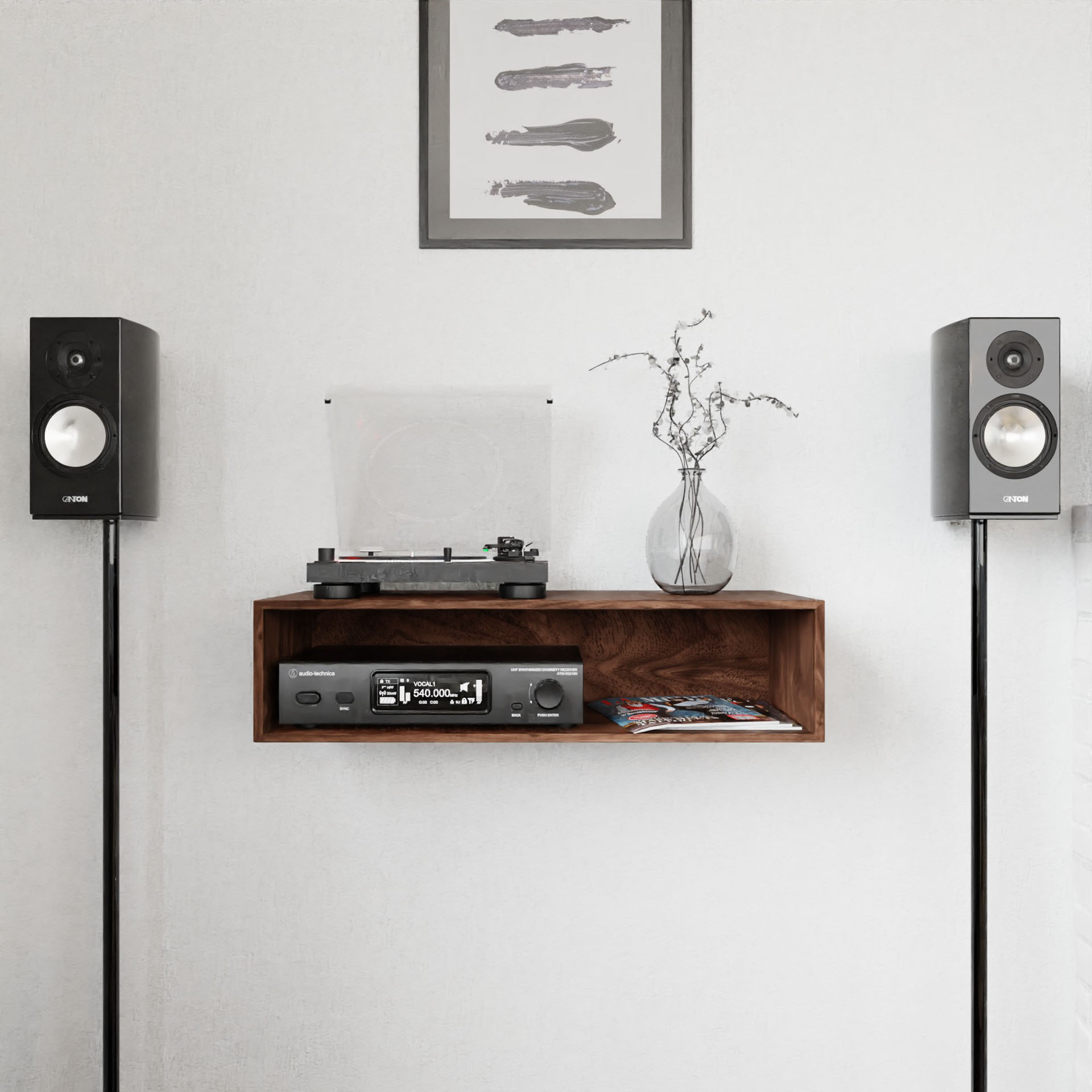 A minimalist audio setup showcases two black speakers on stands next to the Stereo Table in Walnut by Krovel. The table supports a record player with a transparent lid and a stereo receiver, while a vase with branches and framed abstract art elegantly enhance the wall above.